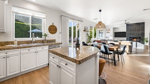 A modern kitchen with white cabinets, granite countertops, and a dining area with a wooden table and chairs. - Wren by Nest Villas | Private Pool, Spa & Firepit (Indio)