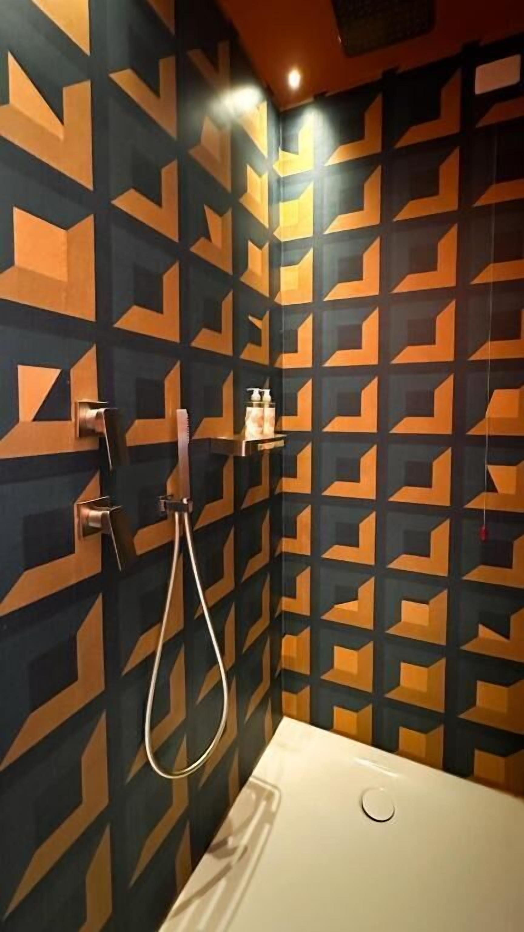 Une salle de bain avec un mur orné d’un motif géométrique, un lavabo blanc et une douchette à main.