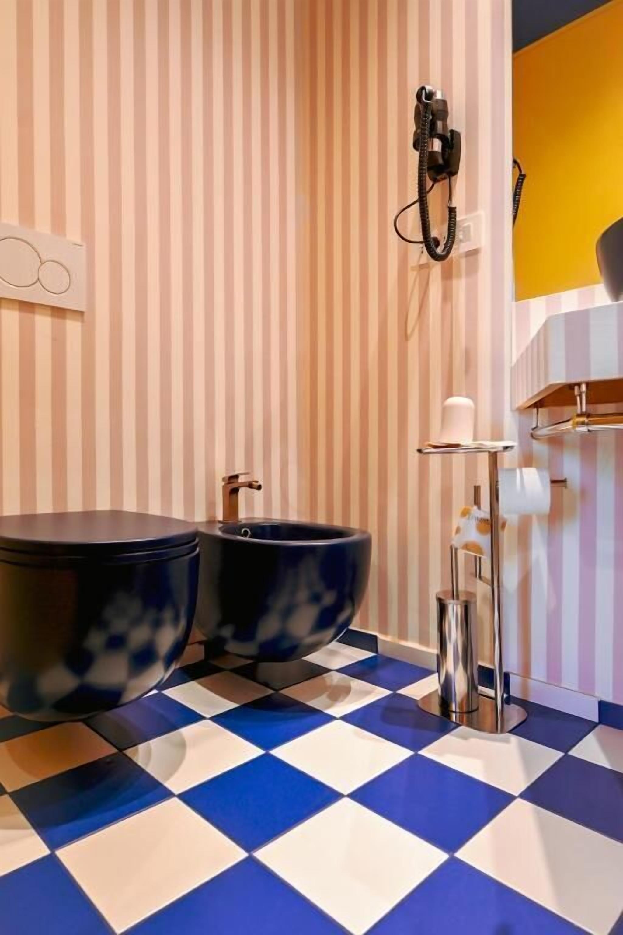 Ein Badezimmer mit gestreifter Wand, einem karierten Boden, einer Toilette, einem Bidet und einem Telefon.