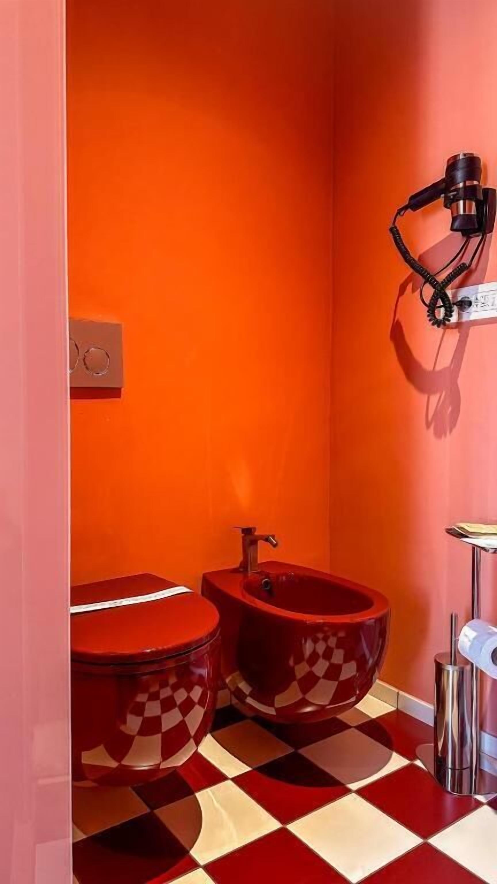 Ein Badezimmer mit zwei roten Toiletten, einem roten Bidet und einem schwarzen Mikrofon an der Wand.