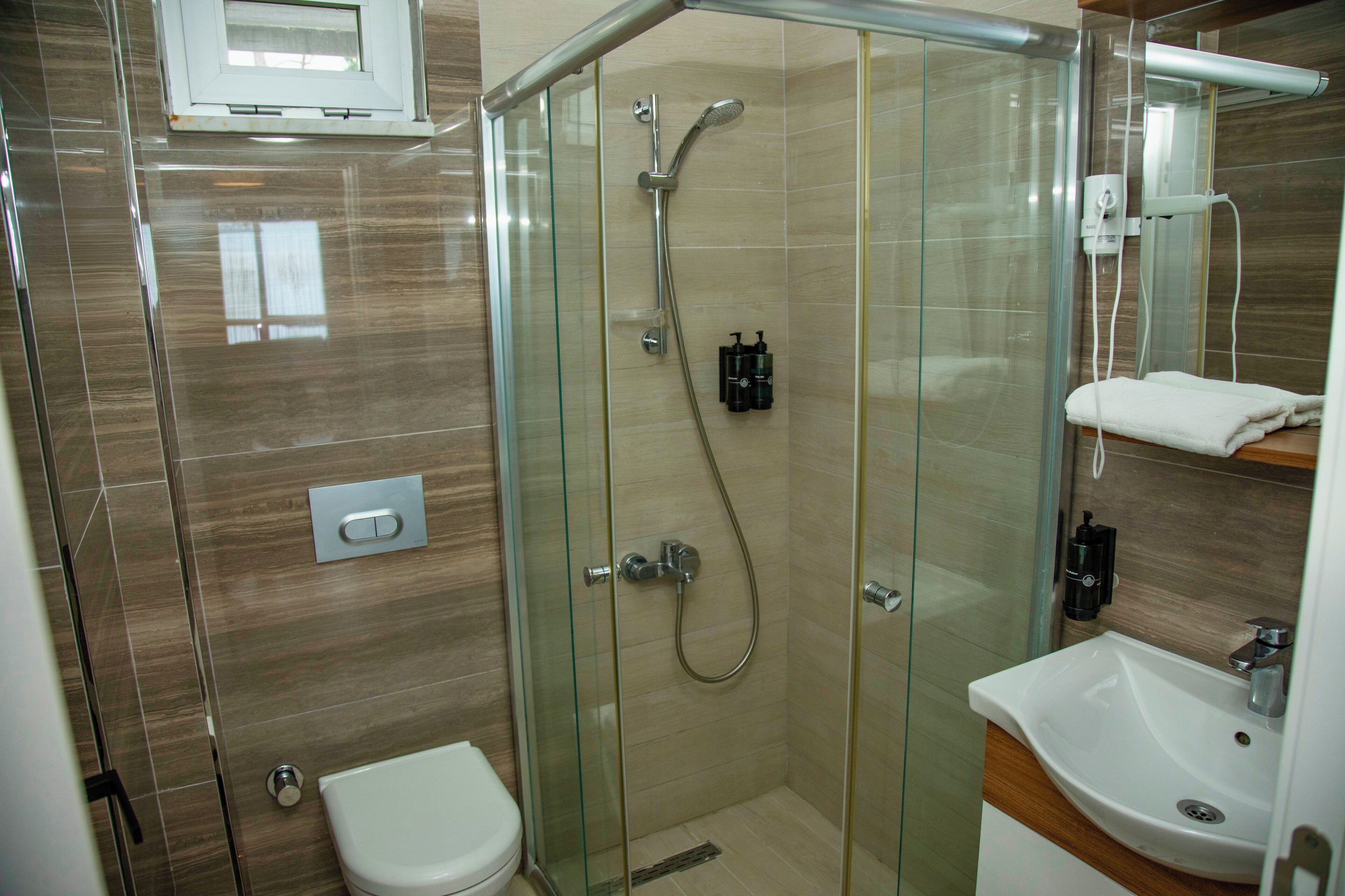 A modern bathroom with a glass-enclosed shower, a white toilet, and a sink with a mirror above it.