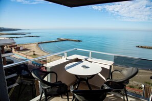 A balcony with a table and chairs overlooking a beach and calm sea. - Sofia Beach Residence (Trabzon)