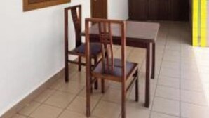 A room with a wooden table and chairs, a window with wooden shutters, and a tiled floor.