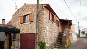 Un bâtiment en pierre avec une porte rouge, des volets en bois et un petit escalier menant à un deuxième étage.