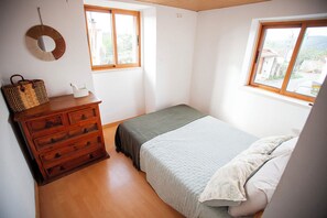 Un dormitorio con un aparador de madera, una cama con colcha a rayas y dos ventanas que dejan entrar luz natural.
