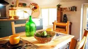 Une table à manger avec un saladier rempli d’avocats, une bouteille verte et un gobelet jaune.