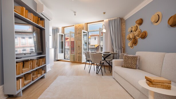 A modern living room with a sofa, dining table, and chairs. There is a bookshelf filled with books and a wall with hats. - Charming Studio for 4 in Historical Center (Oporto)