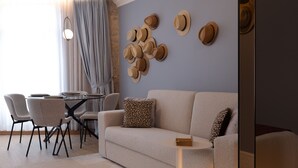 A modern living room with a beige sofa, a dining table with chairs, and a wall decorated with hats. - Charming Studio for 4 in Historical Center (Oporto)