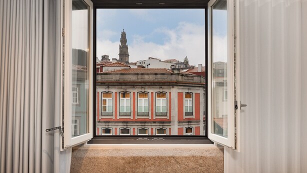 Una stanza con una grande finestra che si apre su un panorama urbano, con una torre imponente e edifici con tetti rossi.