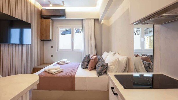 Een moderne hotelkamer met een bed, een flatscreen televisie, een ingebouwd fornuis en een raam met gordijnen.