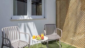 Een klein terras met twee stoelen en een tafel, een raam en een houten schutting.