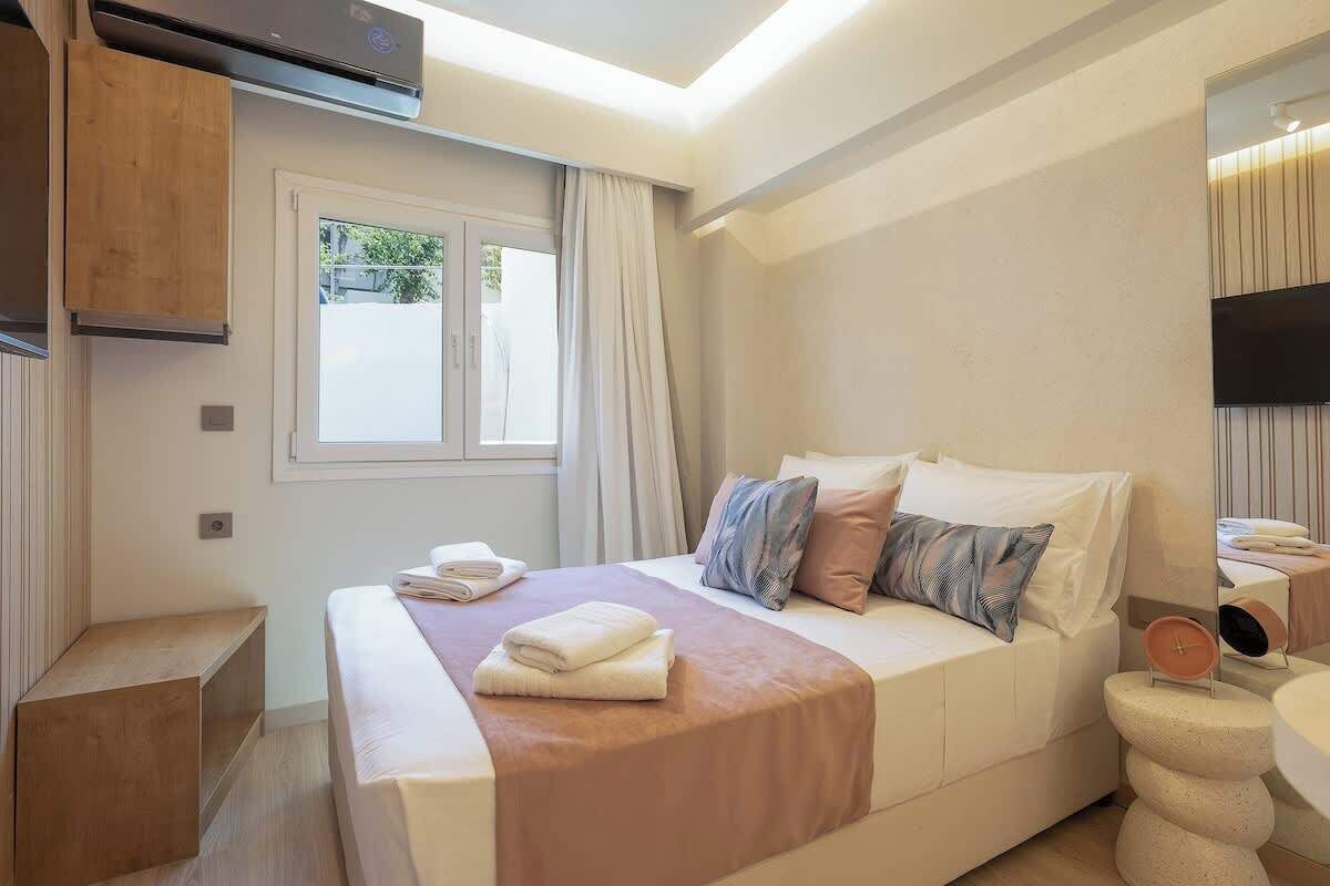 A modern hotel room with a bed, a bedside table, a mirror, and a window.
