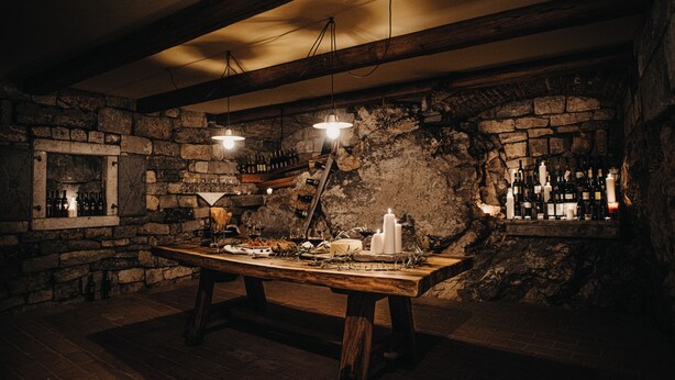 A rustic cellar with a wooden table set for dining, stone walls, and a wine rack. - Hisa Krasna (Sežana)