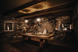 A rustic cellar with a wooden table set for dining, stone walls, and a wine rack. - Hisa Krasna (Sežana)