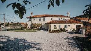 A two-story house with a tiled roof, a gravel driveway, and a small garden with shrubs and a tree. - Hisa Krasna (Sežana)