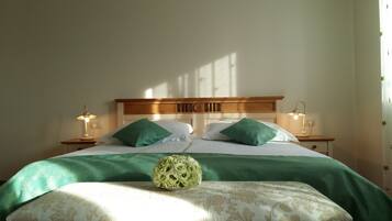 Una cama bien hecha con ropa de cama y almohadas verdes, dos lámparas de noche y un arreglo floral sobre la cama.