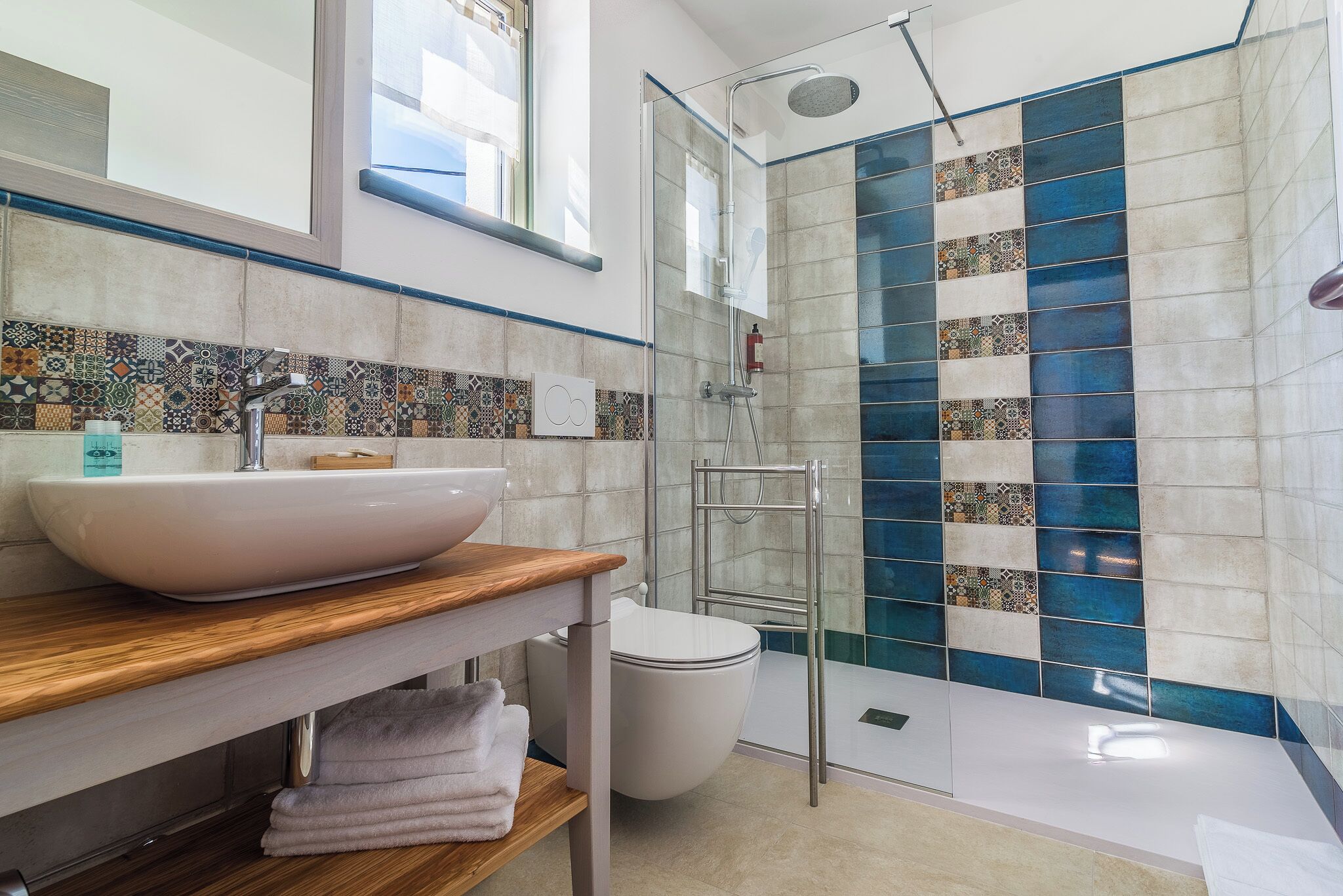 A bathroom with a white sink, a wooden countertop, a glass shower enclosure, and a tiled wall with a blue and beige pattern.