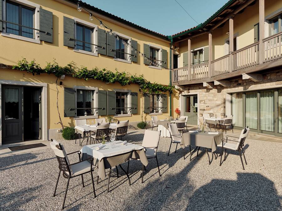An outdoor patio area with tables and chairs, a stone building with balconies, and a clear sky.