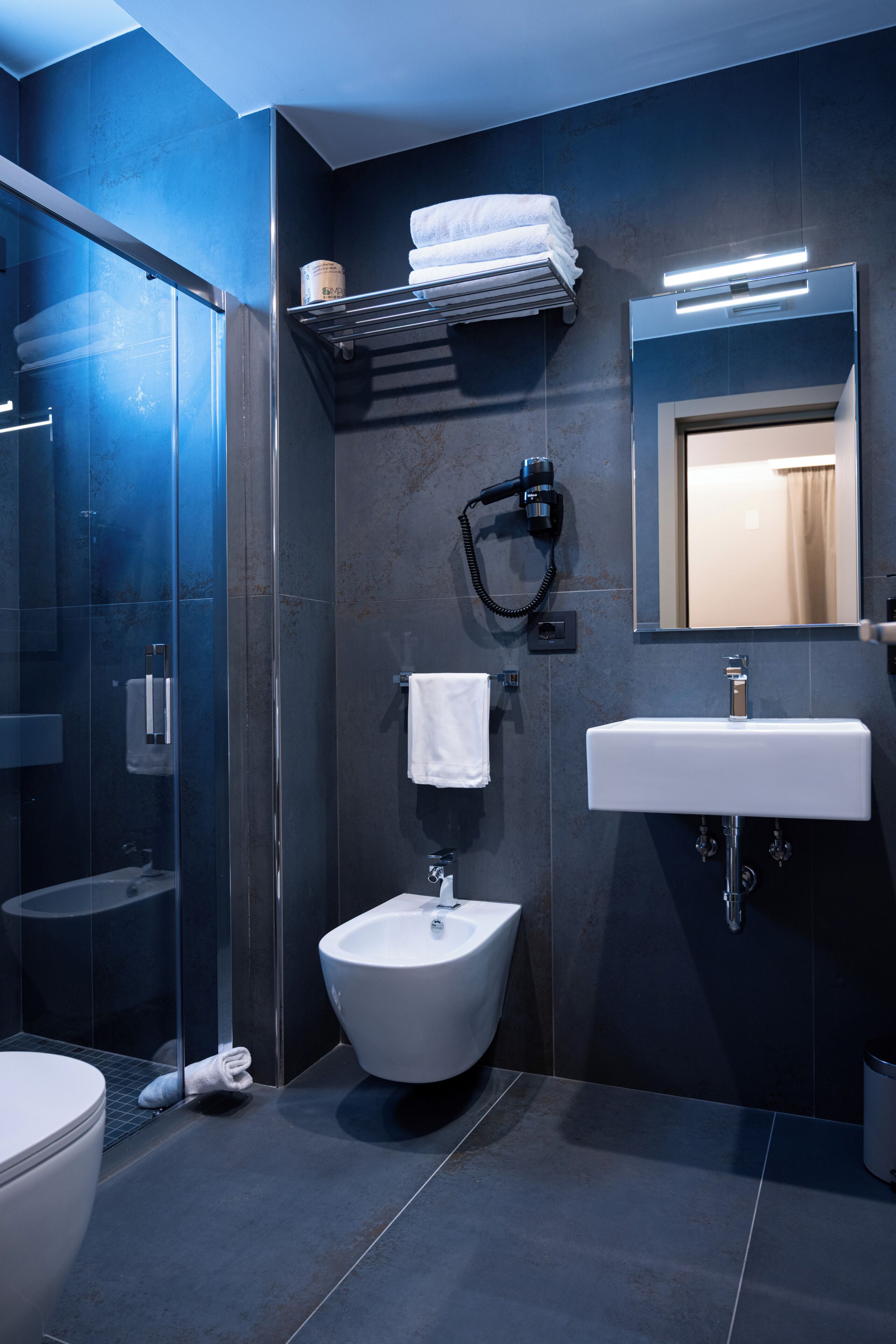 A modern bathroom with a glass shower enclosure, a white pedestal sink, and a bidet.