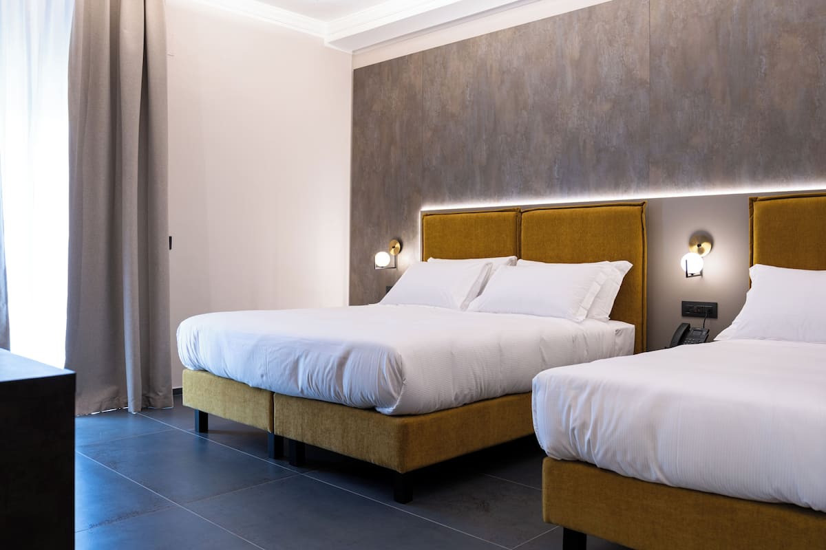 Une chambre d’hôtel avec deux lits, un bureau et une grande fenêtre avec des rideaux.