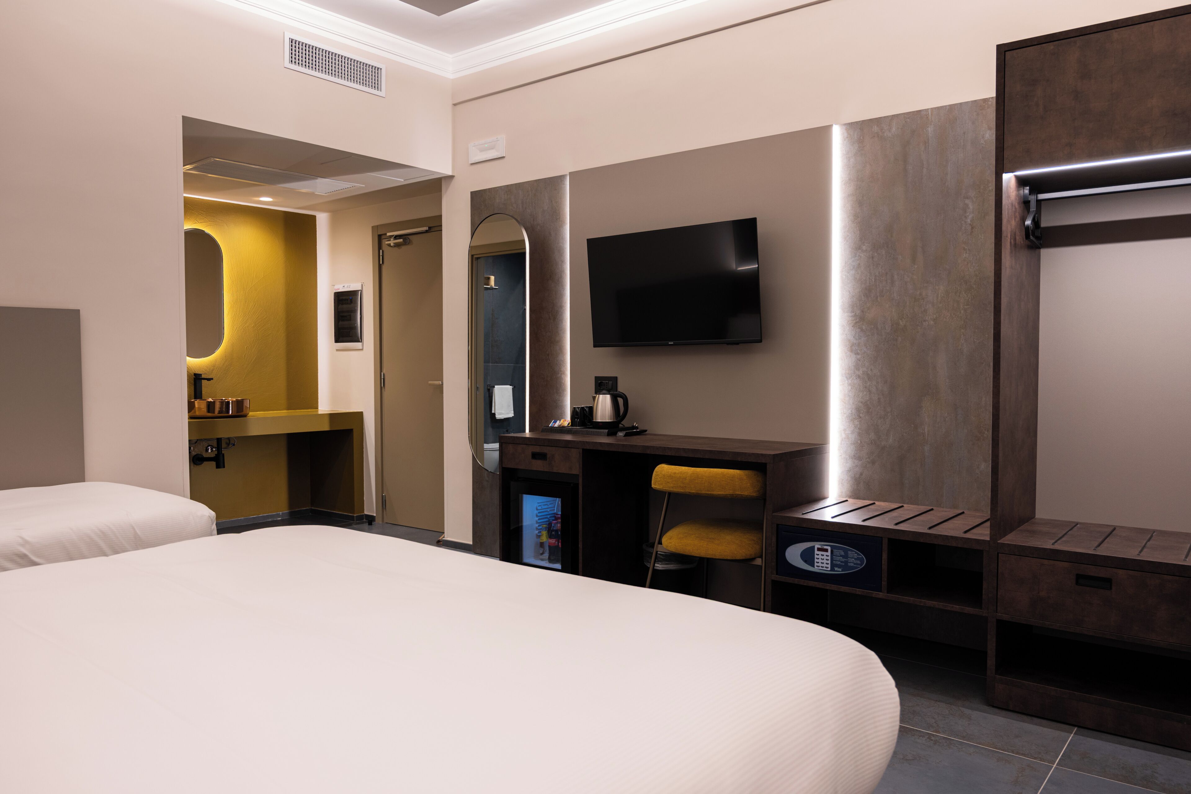 Ein Hotelzimmer mit Bett, Schreibtisch mit Stuhl, Fernseher, Spiegel und Minibar.