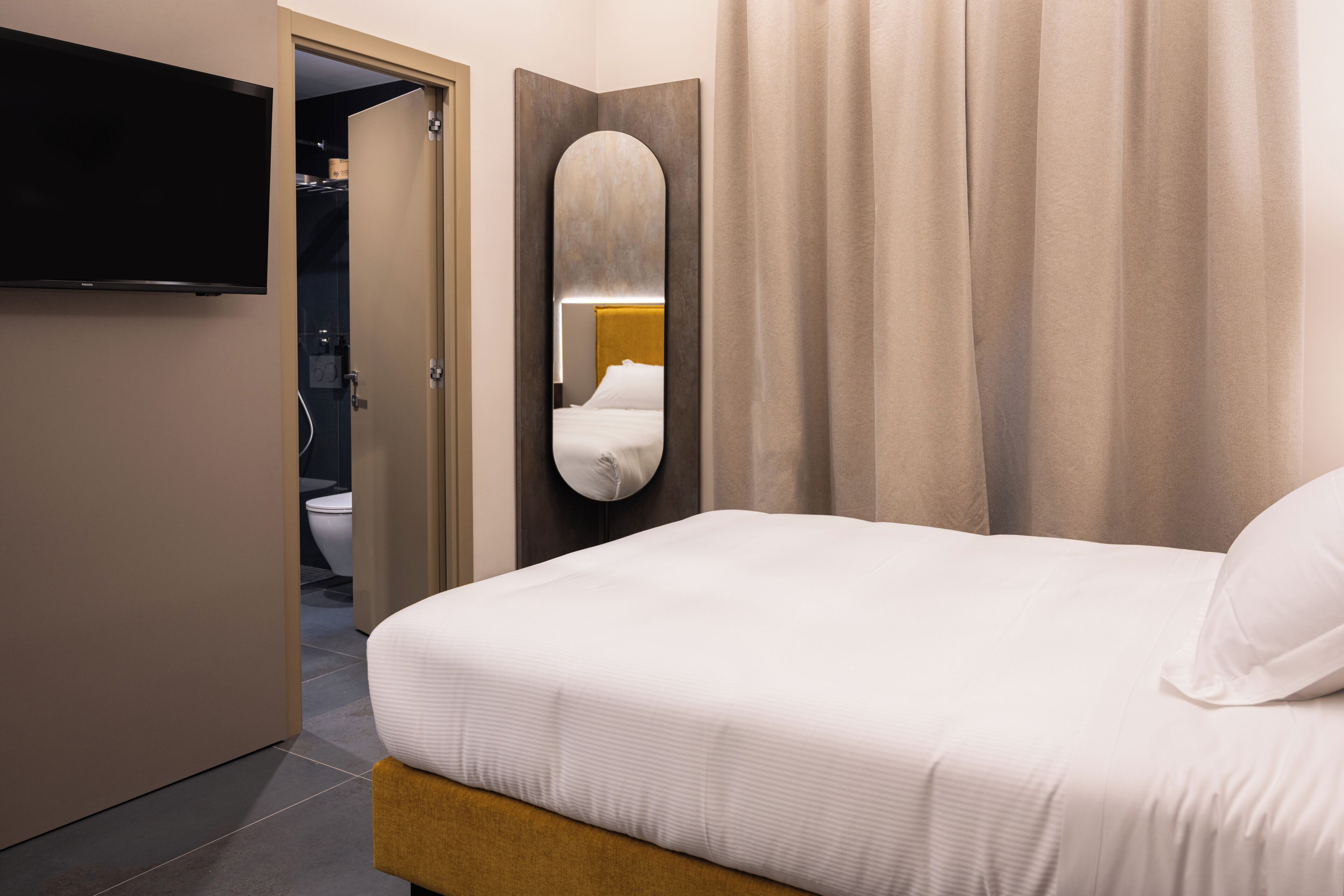 Ein Hotelzimmer mit Bett, Fernseher, Spiegel und einem durch eine offene Tür einsehbaren Badezimmer.