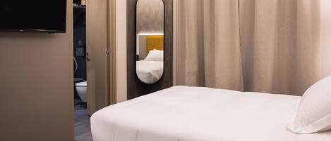 A hotel room with a bed, a television, a mirror, and a bathroom visible through an open door.