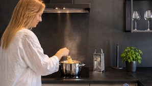 Una cocina moderna con una persona cocinando, un rallador y una planta en maceta.