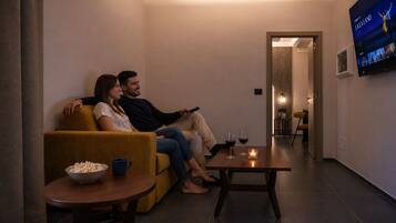 Una pareja sentada en un sofá mirando televisión en una sala de estar moderna, con una mesita y un tazón de palomitas.