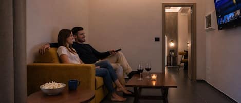 A couple sitting on a sofa watching TV in a modern living room with a small table and a bowl of popcorn.