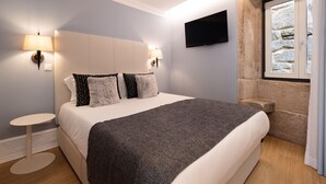 A neatly arranged bedroom with a bed, two bedside tables, a wall-mounted TV, and a stone wall. - Comfy 3BR Duplex in Historical Center (Oporto)