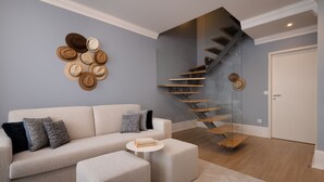 A modern living room with a sofa, ottoman, and a glass staircase leading to a door. - Comfy 3BR Duplex in Historical Center (Oporto)
