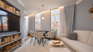 A modern living room with a flat-screen TV, a sofa, a coffee table, and a dining area with chairs and a table. - Comfy 3BR Duplex in Historical Center (Oporto)