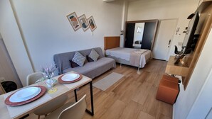 A modern living room with a sofa, a dining table with chairs, a small bed, and a kitchenette. - Studio 325 Teresópolis - Best Location.  WATERFALLS AND GASTRONOMY (Teresópolis)