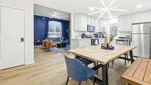 Une cuisine moderne avec des meubles blancs, un réfrigérateur en acier inoxydable et une table à manger en bois.