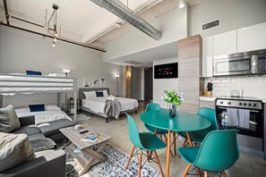 Ett modernt hotellrum med en våningssäng, en soffa, ett matbord med stolar, ett köksutrymme med mikrovågsugn och ugn samt en platt-TV på väggen.
