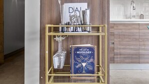Et moderne køkken med træskabe, en stålvask og en guldfarvet metalkonstruktion, der viser en bog med titlen "The Art of Mixology" samt forskellige køkkenredskaber.
