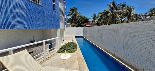 A swimming pool with a tiled wall on one side and a building with blue tiles on the other. - COPIA0104 - Torre Piatã Residence (Salvador)