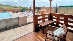 Une terrasse couverte avec un plancher en bois, une piscine et un espace détente comprenant un banc et une table.