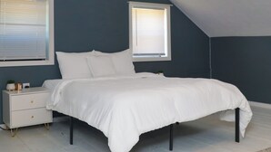 Una camera da letto con un letto, un comodino bianco e due finestre con tende.