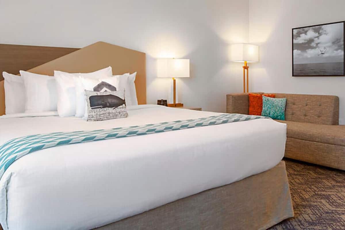 Hotellihuone, jossa on suuri sänky, sohva, kaksi yöpöytälamppua ja seinällä oleva kehystetty taulu.