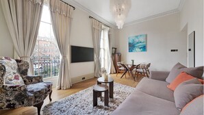 A living room with a sofa, a patterned armchair, a dining table with chairs, a chandelier, and a painting on the wall. - Compton Terrace N1 🚇 Highbury and Islignton (London)