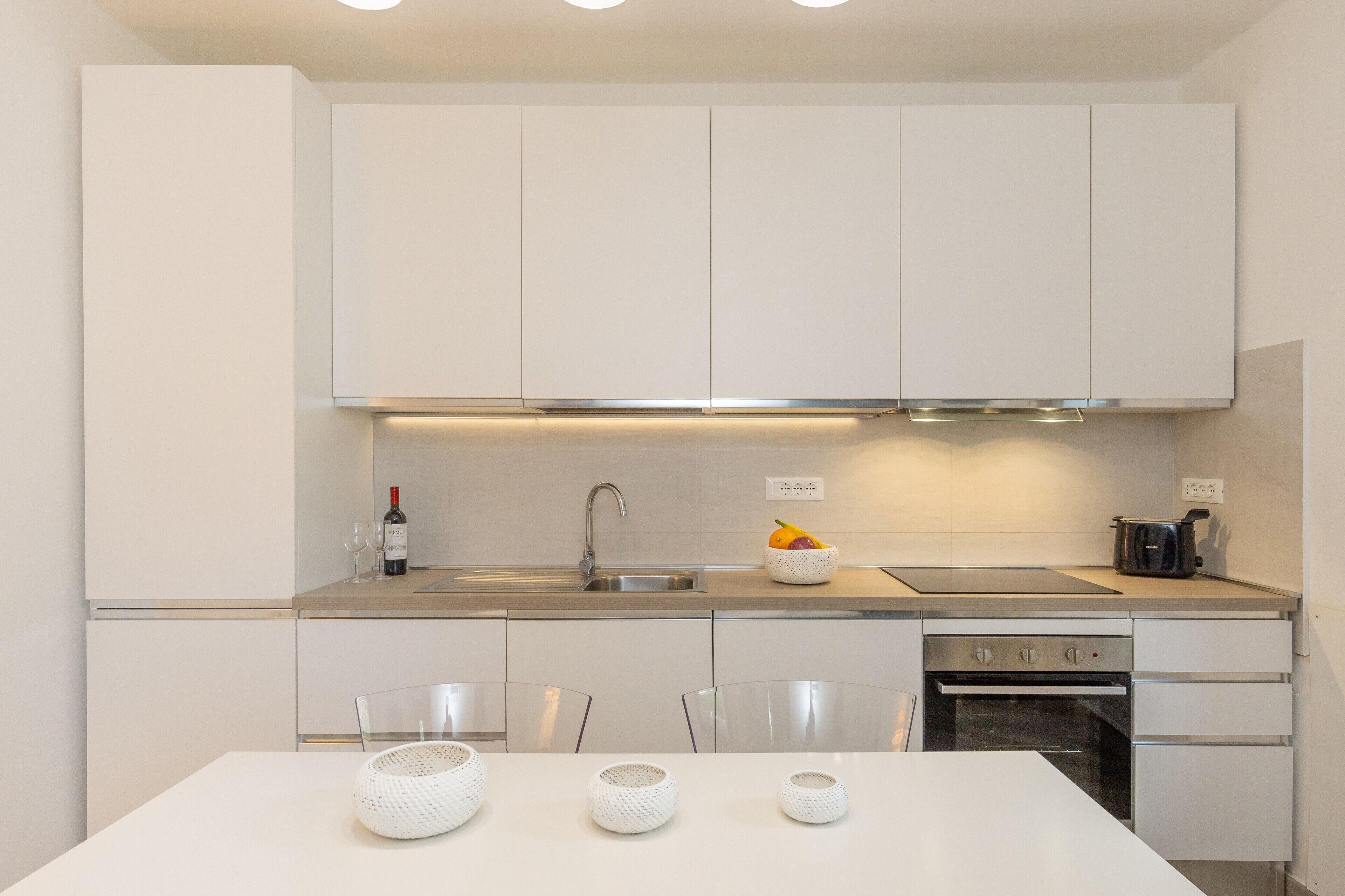 Une cuisine moderne avec des meubles blancs, un évier en acier inoxydable, une cuisinière à gaz et un lave-vaisselle.
