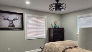 Un dormitorio con cama, cómoda, ventilador de techo e imagen enmarcada de un ciervo.