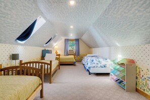 A cozy attic bedroom with two beds, a desk, and a window with curtains. - Alden East Torch Estate (Alden)