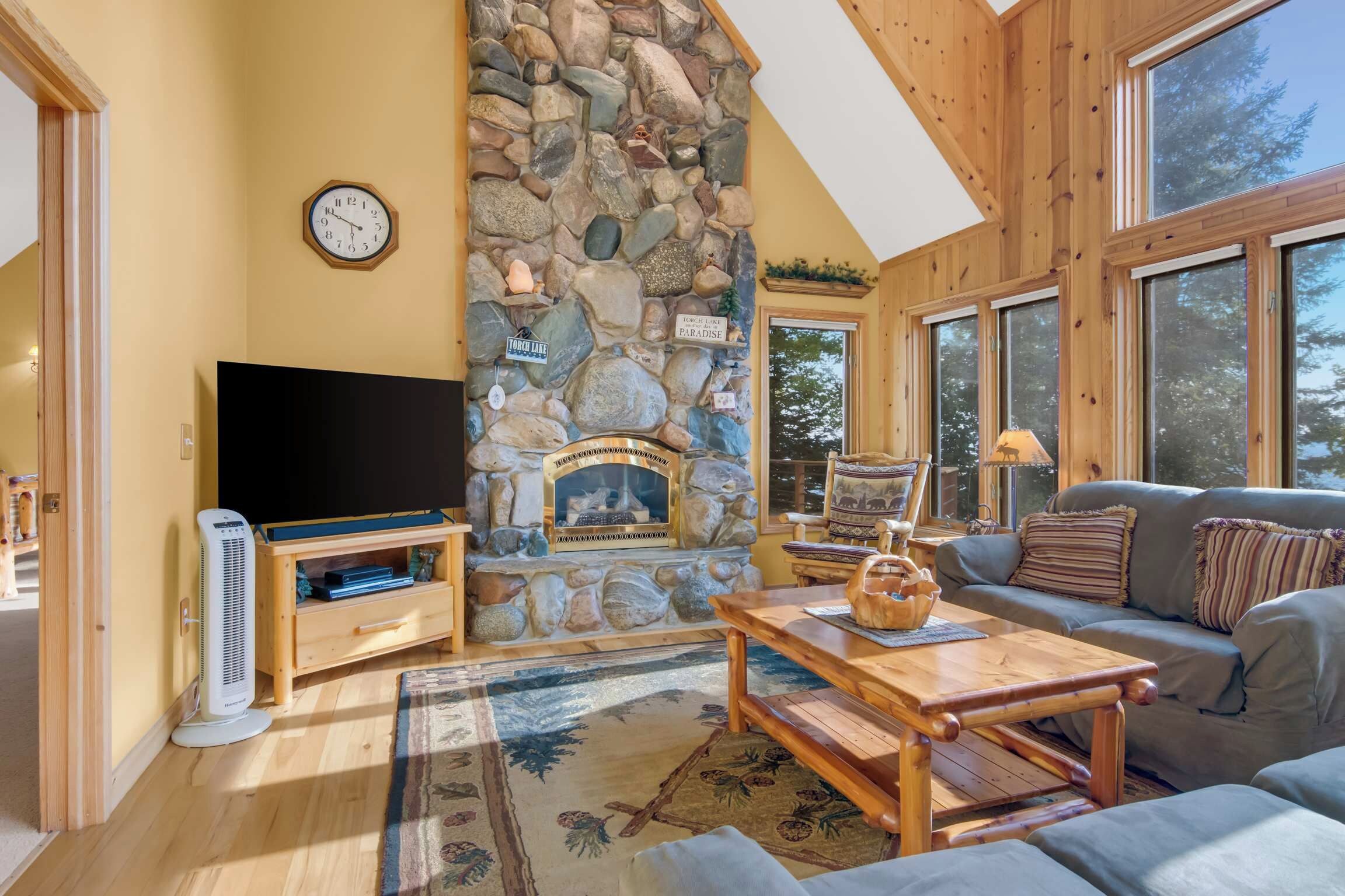 A cozy living room with a stone fireplace, a flat-screen TV, a sofa, and a coffee table.