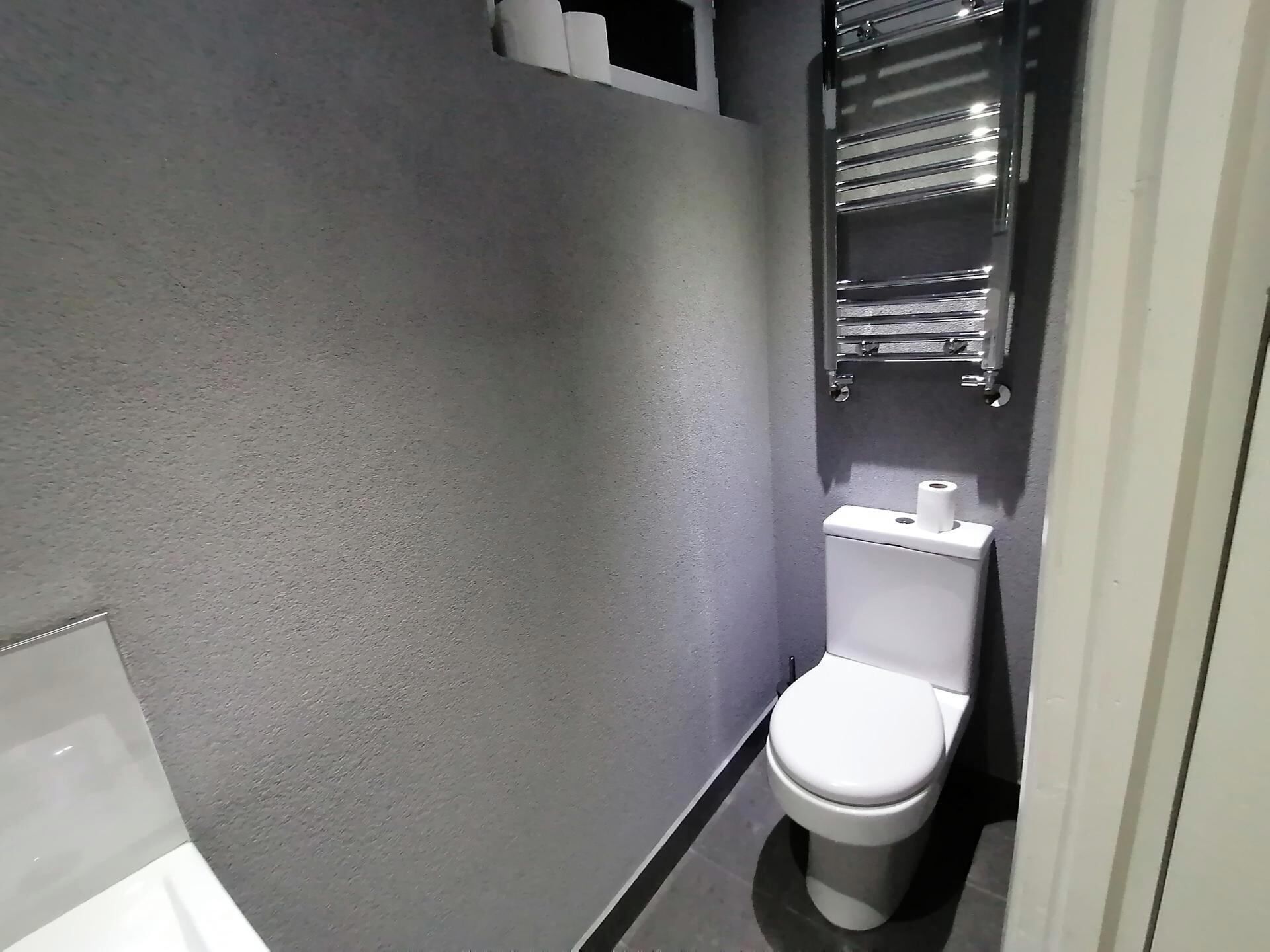 Un bagno piccolo e moderno con il water bianco, un portasciuga e un portasciugamani.