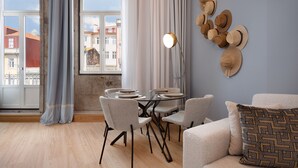 A dining area with a round table, chairs, and a view of buildings through large windows. - Sweet Studio for 4 in Historical Center (Oporto)
