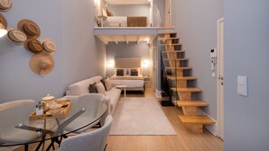 A compact living space with a loft bedroom, a dining area with a glass table, and a staircase. - Sweet Studio for 4 in Historical Center (Oporto)