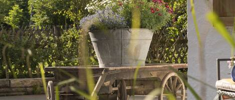 A garden cart with a flower pot on a paved surface, surrounded by greenery.